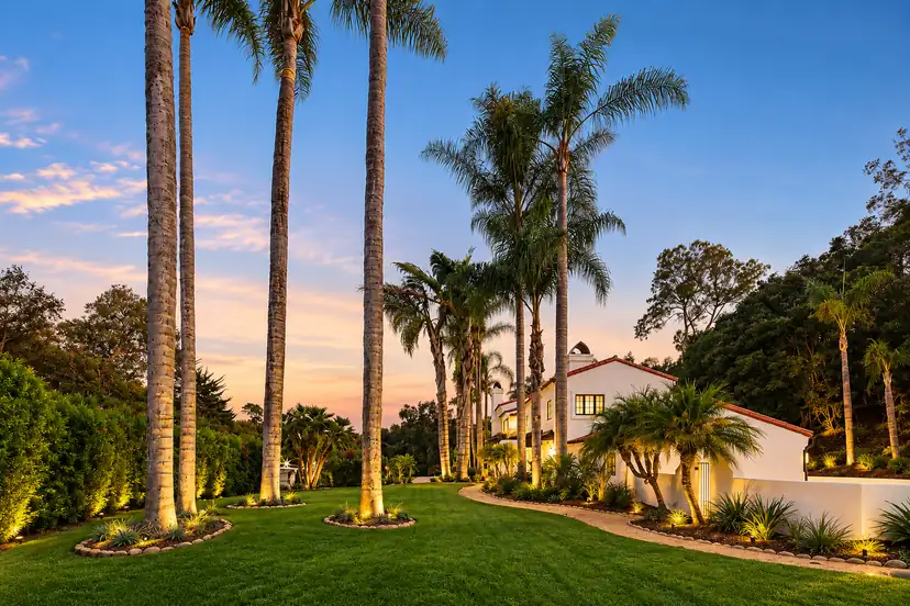 Santa Barbara estate with illuminated palm trees and manicured lawn at twilight, landscaped by Reyes Gardening Services